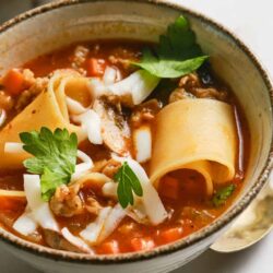 Savory homemade beef and vegetable lasagna soup in a rustic bowl with herbs.