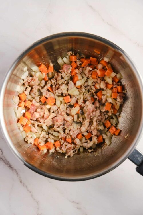 Sautéed ground turkey with diced onions and carrots in a stainless steel pan.