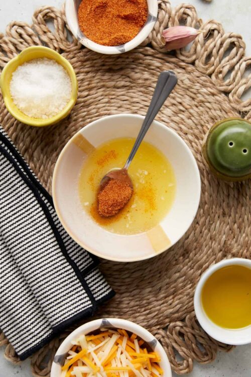 Spice blend in bowl with oil, garlic, salt, and pepper on woven placemat for cooking.