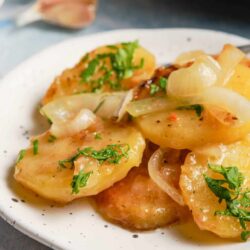 Creamy scalloped potatoes with onions and herbs on a white plate for comfort food.