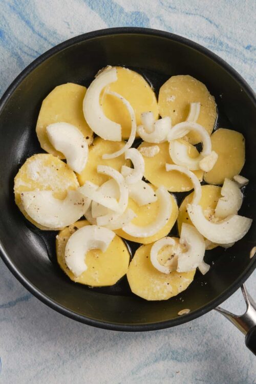 Sliced potatoes and onions in a black skillet for cooking.