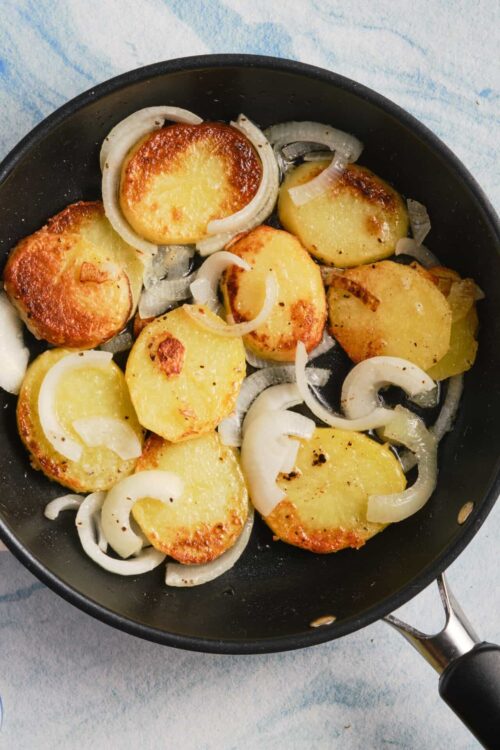 Golden roasted potatoes cooking with sautéed onions in a black skillet.