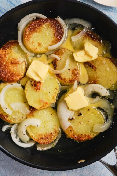 Crispy smashed potatoes with butter and onions in a skillet.