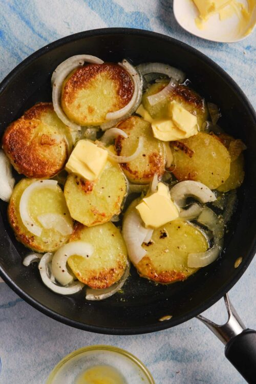 Golden roasted potatoes with onions and butter in a black skillet, ready to serve.