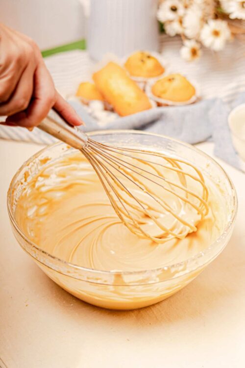 Creamy vanilla frosting in a glass bowl, ready for cake decorating, with baked pastries in the background.