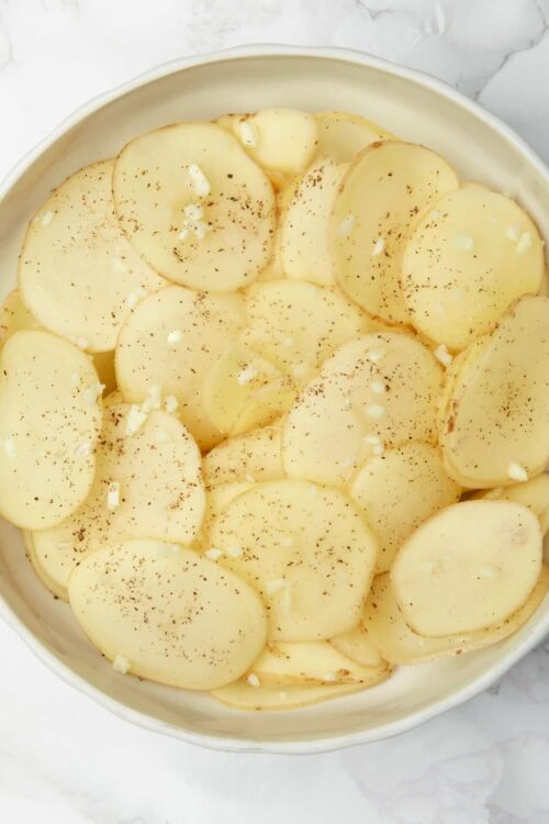 Thinly sliced potatoes in a creamy casserole dish topped with black pepper and cheese.
