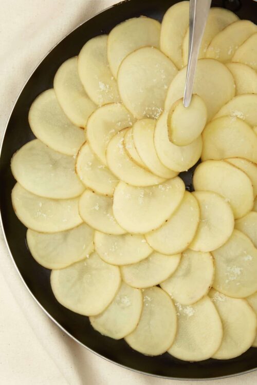 Thinly sliced potatoes layered in a skillet for homemade potato gratin.
