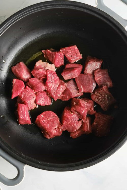 Cubs of raw beef browning in a non-stick skillet for cooking or recipe preparation.