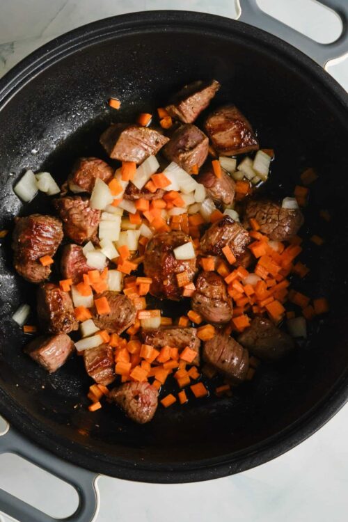 Sautéed beef stew with onions and carrots in a black skillet for comfort food recipe.