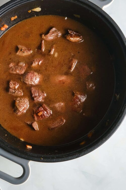 Slow cooker beef stew cooking in a black crockpot with tender beef chunks and flavorful broth.