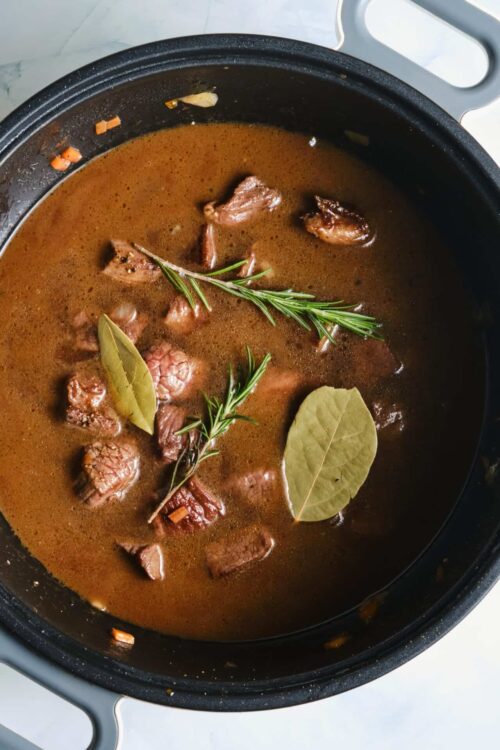 Slow cooker beef stew with fresh herbs and bay leaves in a rich broth.