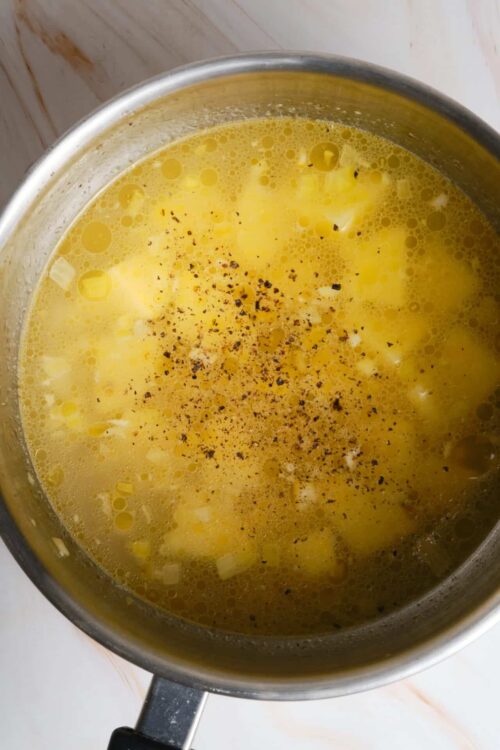Butter and onion mixture in a saucepan with black pepper.
