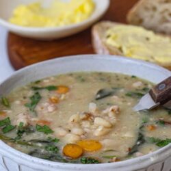 Creamy chicken vegetable soup in a white bowl with herbs and vegetables.