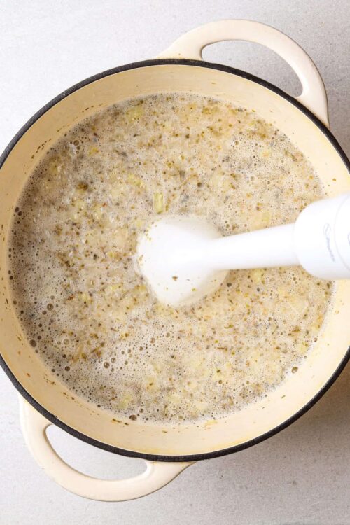 Creamy onion soup cooking in a vintage enamel pot with a white immersion blender.