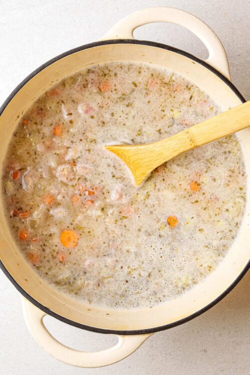 Creamy homemade chicken soup with vegetables in a white pot.