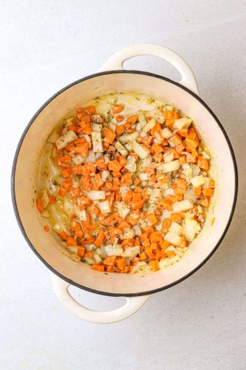 Diced carrots and onions cooking in a yellow cast iron skillet for homemade vegetable sauté.