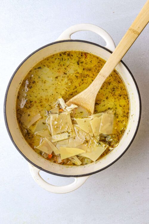 Creamy cheese and vegetable soup in a white enamel pot with a wooden spoon.