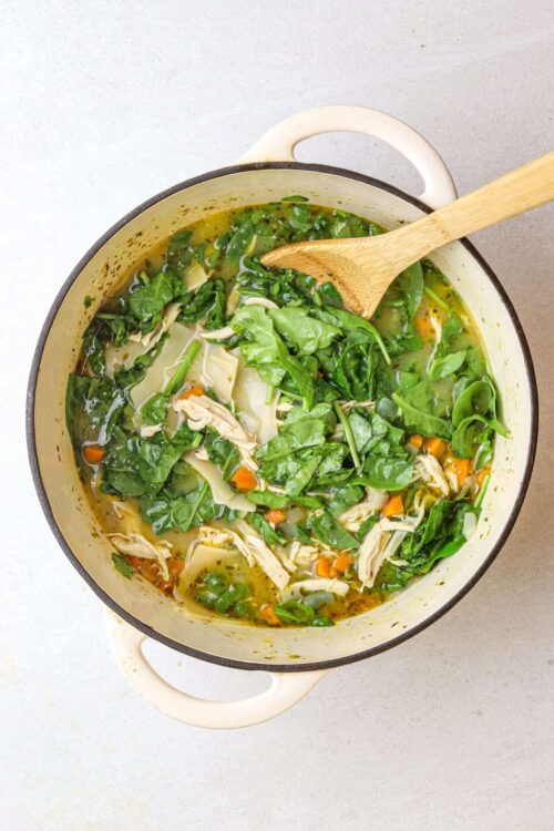 Fresh homemade chicken and vegetable soup in a white enamel pot on a light background, healthy and comforting meal.