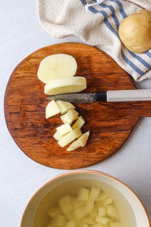Sliced potatoes on a wooden cutting board with a knife, ready for cooking or recipe prep.