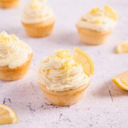 Lemon cupcakes with creamy lemon frosting and lemon slices on white surface.