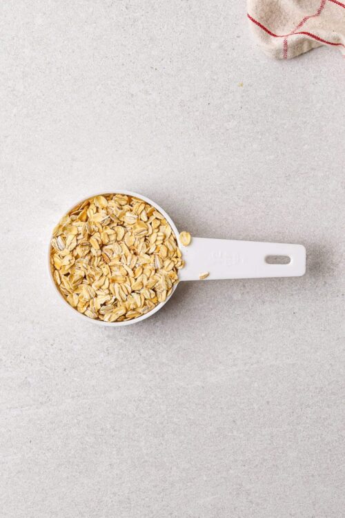 Rolled oats in a white measuring cup on a light gray surface.