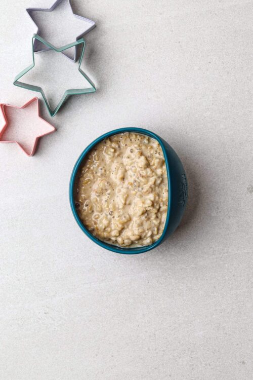 Creamy oatmeal in blue bowl with star-shaped cookie cutters on white countertop.