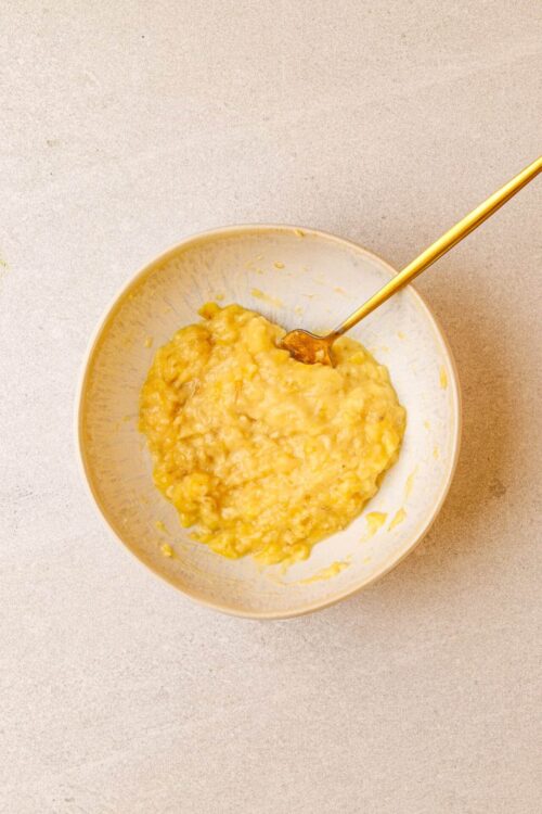 Creamy mashed bananas in a bowl with a spoon for banana recipes and homemade banana mash or baby food.