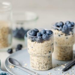Creamy blueberry overnight oats topped with fresh blueberries, served in a glass on a light blue plate.
