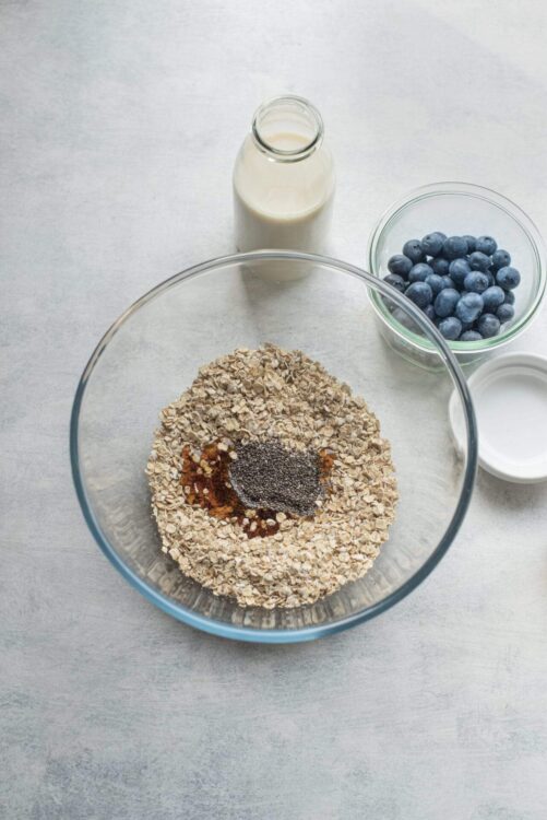 Oatmeal, blueberries, and milk ingredients for healthy breakfast recipe in glass bowls and bottle.