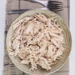 Shredded cooked chicken in a large bowl on a woven cloth, ready for recipes.