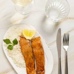 Grilled salmon with lemon, served with rice and parsley on white plate.