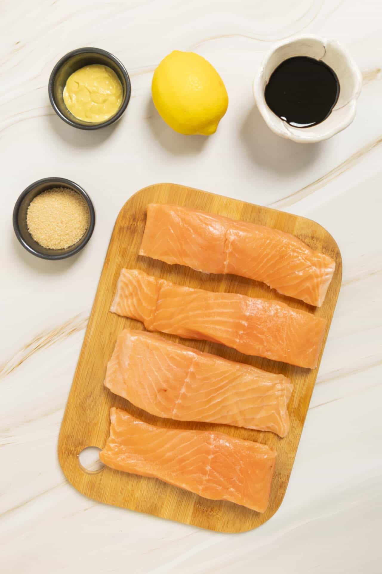 Fresh salmon fillets on a wooden cutting board with lemon, soy sauce, ginger, and mustard, perfect for healthy seafood recipes.