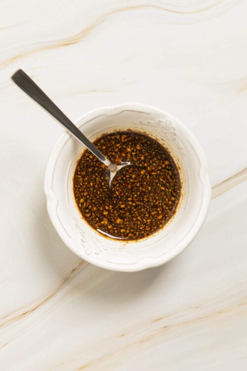 Soy sauce and garlic marinade in a white bowl with a spoon on a light wooden surface.