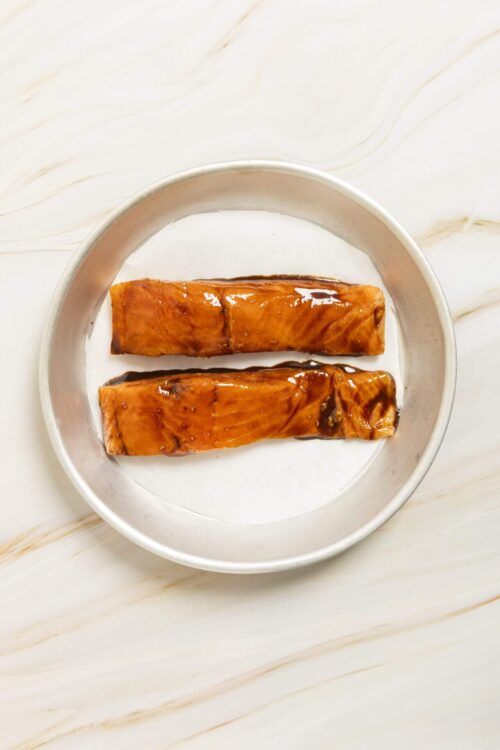 Sweet glazed salmon fillets on a white plate, ready for baking or serving.
