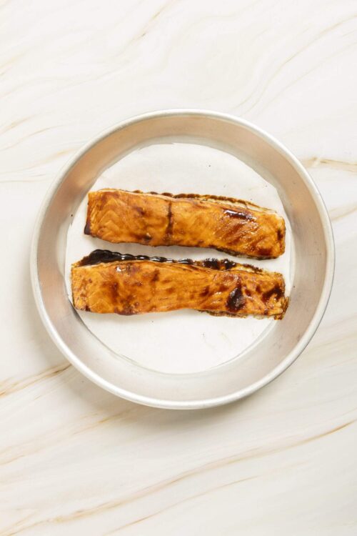 Salmon fillets with teriyaki glaze on a round metal plate.