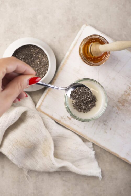 Spoonful of chia seeds being added to a glass of milk or yogurt.