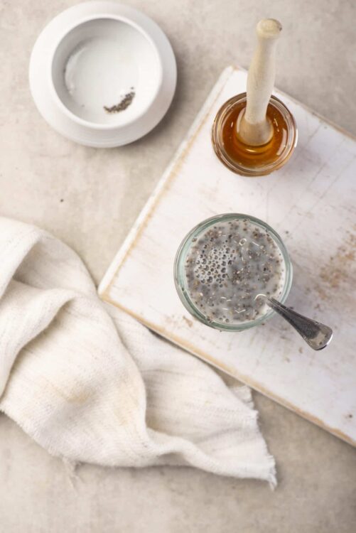 Vanilla chia seed pudding with honey and milk in glass jar on white wooden board.