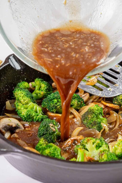 Creamy mushroom and broccoli stir-fry being cooked in a skillet with savory sauce.