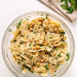 Creamy chickpea pasta salad with herbs in a glass bowl on white background.