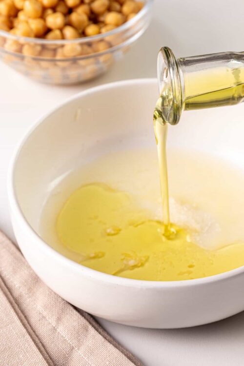Golden olive oil being poured into a white bowl for baking or cooking.