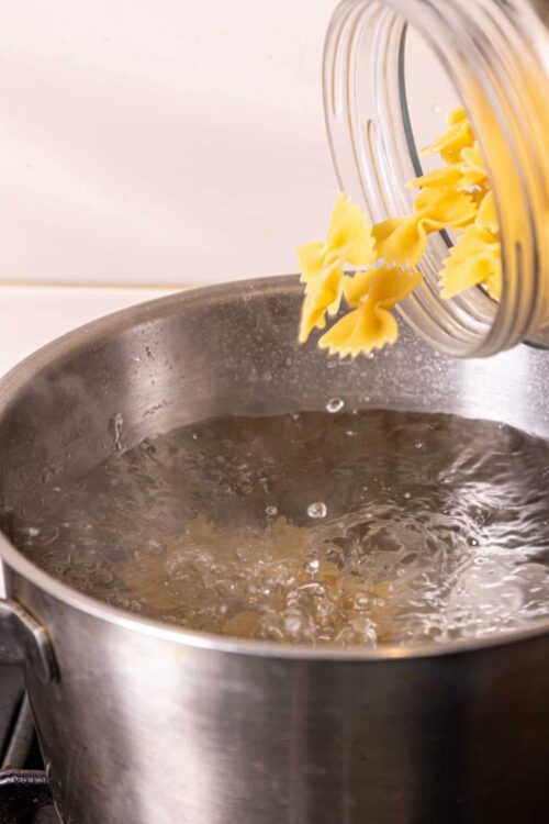 Uncooked pasta being poured into boiling water in a stainless steel pot.