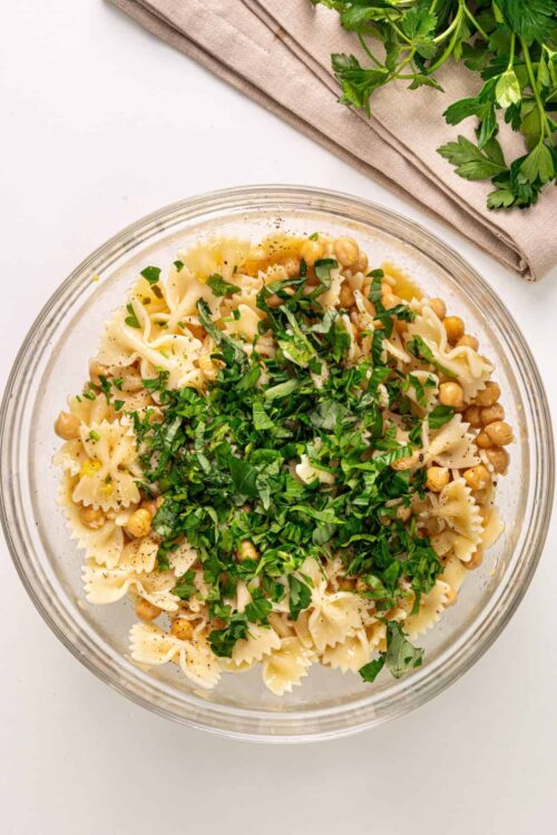 Creamy pasta salad with fresh herbs and chickpeas in a glass bowl.