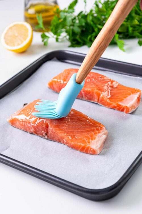Raw salmon fillets on a baking sheet with a silicone basting brush.