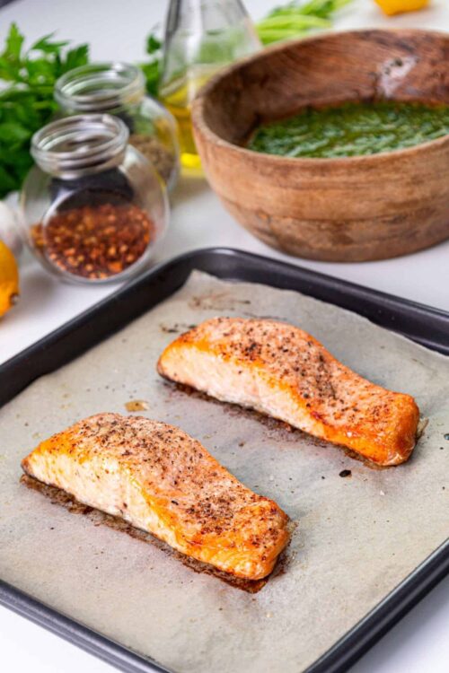 Savory seasoned salmon fillets baking on a parchment-lined sheet pan.