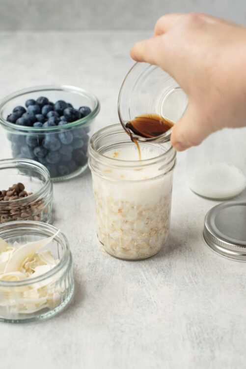 Fresh oatmeal jar with vanilla, blueberries, chocolate chips, and caramel syrup ingredients for baked oatmeal recipe.