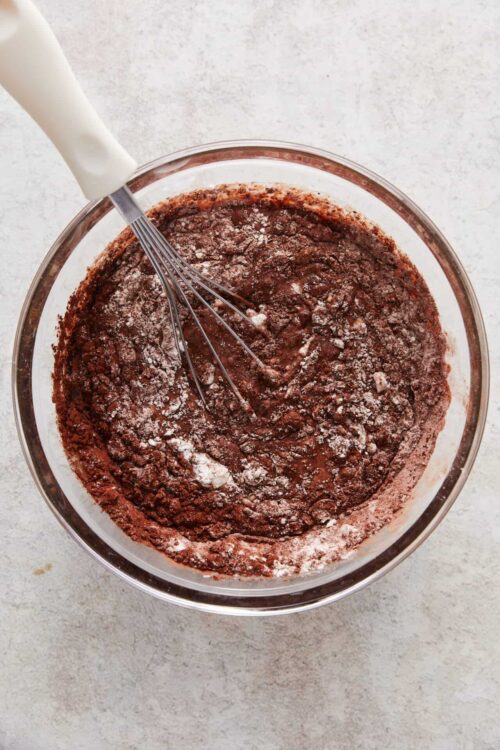Creamy chocolate cake batter in a glass mixing bowl with a whisk.