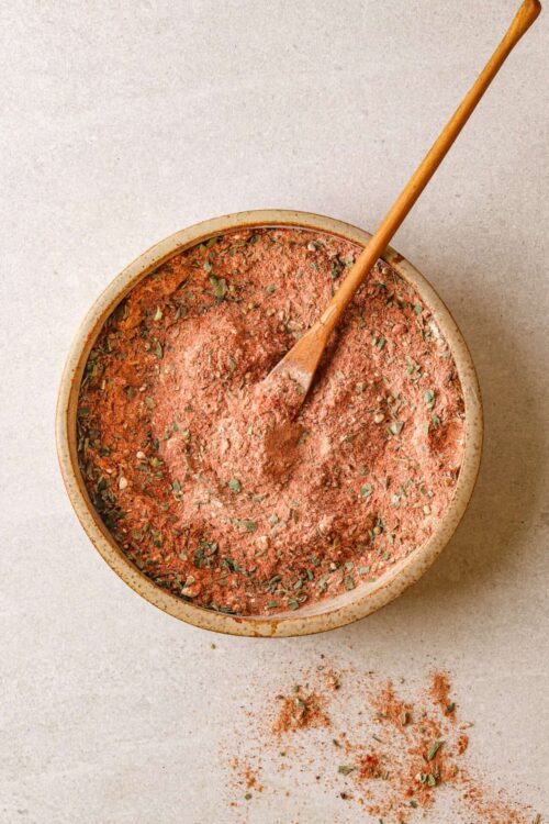 Smoked paprika, herbs, and spices in a bowl with a wooden spoon on a light background.
