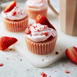 Fresh strawberry cupcakes with whipped frosting and red crumbs on a white surface.