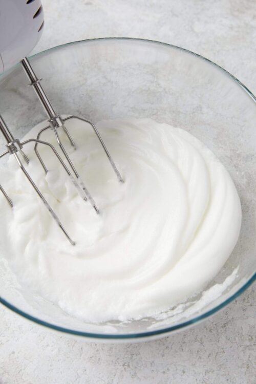 Fluffy whipped cream in a glass mixing bowl with beaters attached.