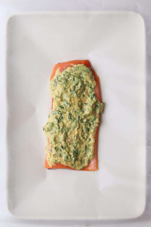 Baked salmon with avocado herb sauce on white baking tray, healthy and delicious seafood dish.